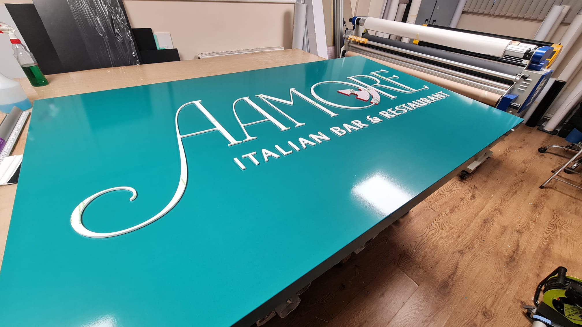 Teal gloss acrylic sign panel for Aamore Italian Bar and Restaurant with raised white lettering, in production at Deco Studio Bristol workshop