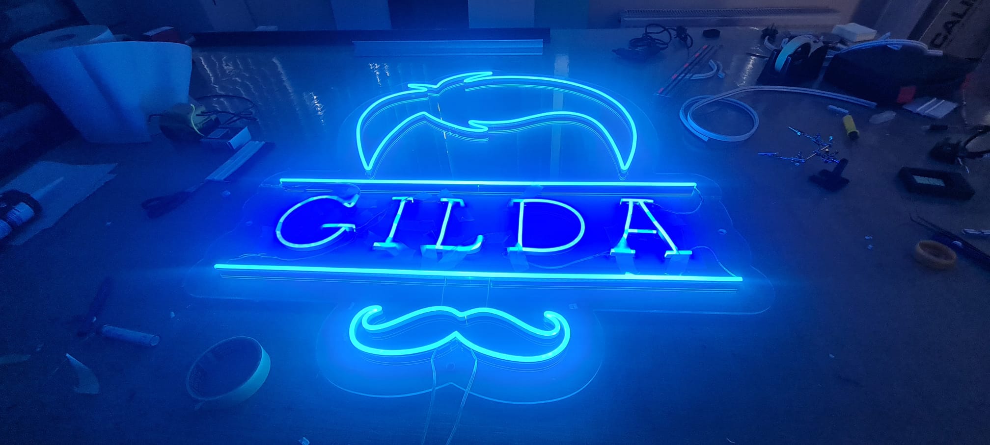 Custom blue LED neon-effect acrylic sign for Gilda barbershop with moustache and hair motif, made by Deco Studio Bristol